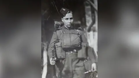 A young boy in army uniform pictured in black and white. 