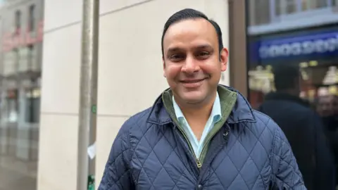 Andy Mohinta, in a blue coat and shirt, is smiling at the camera.
