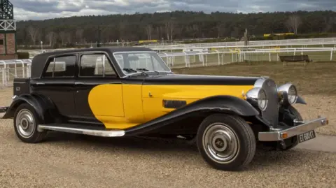 Osenat Johnny Hallyday's black and yellow 1975 Panther De Ville car which has a long bonnet, a silver bumper and tires with Hallyday's initials sitting in a farm.