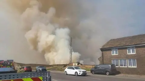 Derbyshire Fire and Rescue Service Smoke rising over the moors with a road, cars and a small building in the foreground