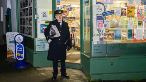 Jack Boskett A picture of a railway staff worker wearing a black hat and black jacket. He is pictured in front of a green store which reads 'Bridgetown stores'