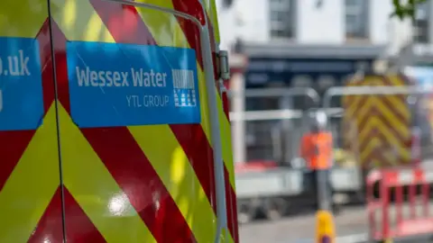 A yellow and red striped van with the Wessex Water logo on it set against a blurred background of a high street.