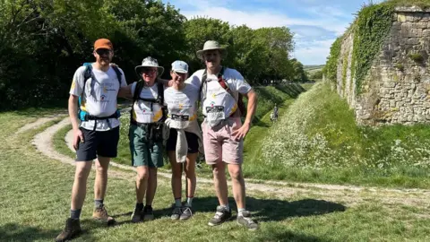 Debs Goodenough posing with her sons and daughter-in-law next to stone ruins surrounded by a grass moat.
