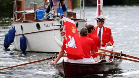 Rowing boat with four swan uppers wearing red tops and white trousers onboard rowing on the Thames