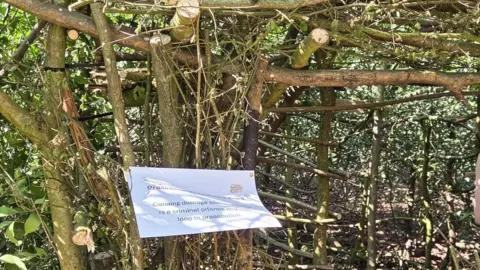 Friends of Chaddesden Wood A wooden den with a warning sign hung from it which warns of prosecution to anyone who damages the woodland.