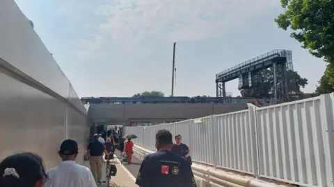 A view of the southern walkway which opened on 17 July, running from Frideswide Square to the Westgate Hotel. Several people are walking along it, some with bicycles. A train is seen on the rail bridge above them.