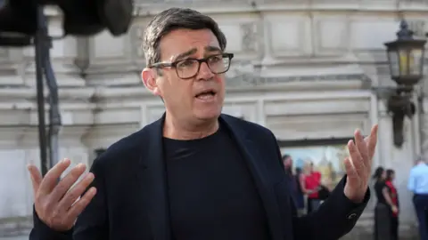 PA Media Andy Burnham Mayor of Greater Manchester speaks to the media outside Central Hall in Westminster. He is wearing a black blazer and t-shirt, and black glasses with his hands held aloft.