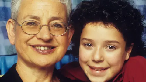 A picture of Jacqueline Wilson with young Dani Harmer, as Tracy Beaker. They're smiling.