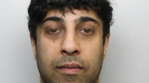 A mugshot of Wiqas Mahmud. He has black hair and facial stubble.