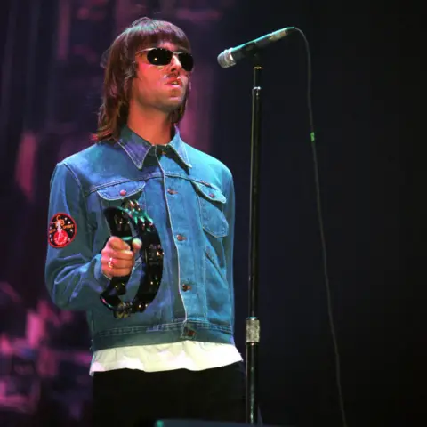 Getty Images Liam Gallagher performing at Glasgow Green, on stage wearing a blue denim jacket holding a tamborine