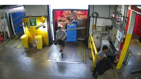 Three men appear from the inside of a trailer as they enter a warehouse.