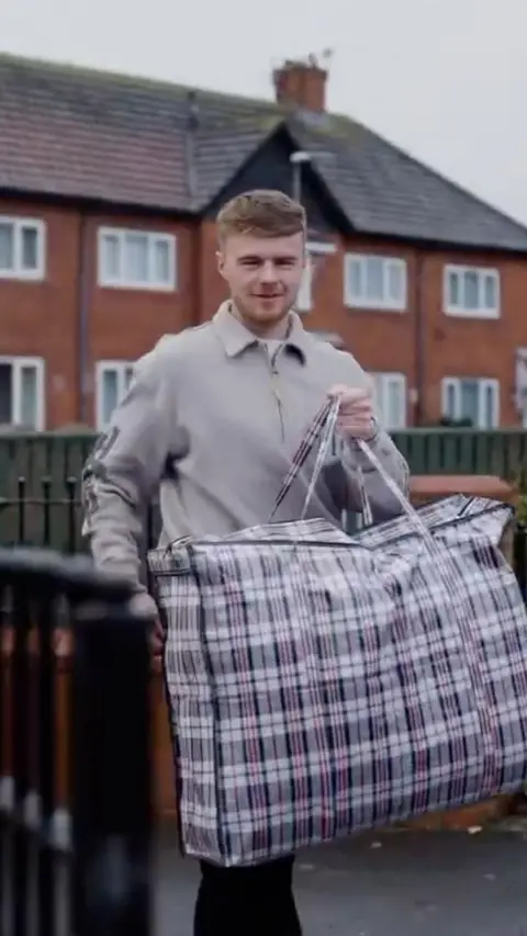 Middlesbrough footballer Tommy Conway carrying a check bag infront of a row of terraced houses