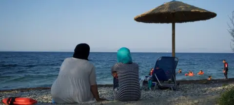 Proem-aid Women look on from the beach