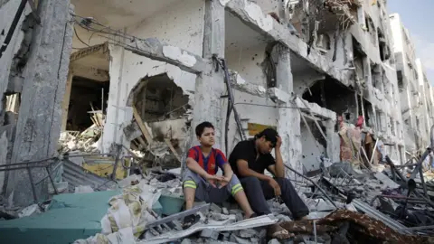 Reuters Palestinians sit on the remains of their destroyed homes in Beit Hanoun, Gaza (5 August 2014)
