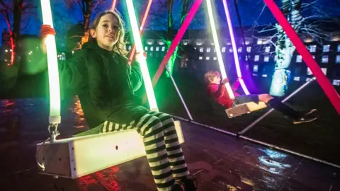 ANDRE PATTENDEN Two children on a light-up swing installation