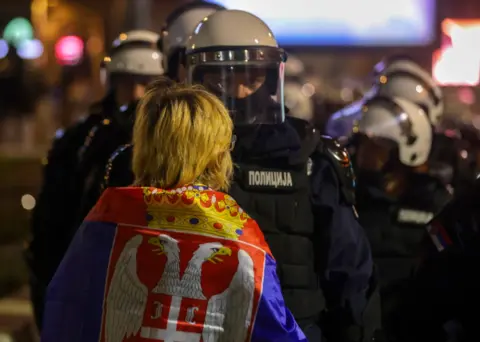 EPA Back of female protestors head. She is wearing Serbian flag draped over her shoulders and faced with a policeman in riot gear.