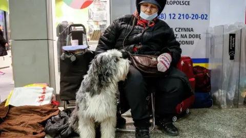 Getty Images An elderly woman sits with her dog at a rail station