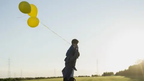 Getty Images A man with a boy on his shoulders, holding balloons