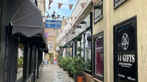 BBC A photo showing a street in Gloucester with shops on either side and bunting stretching across from the buildings. In the background is Gloucester Cathedral