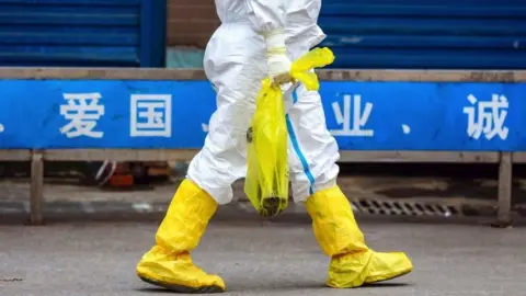 Getty Images Worker walking past Huanan market with white hazmat suit and yellow boots