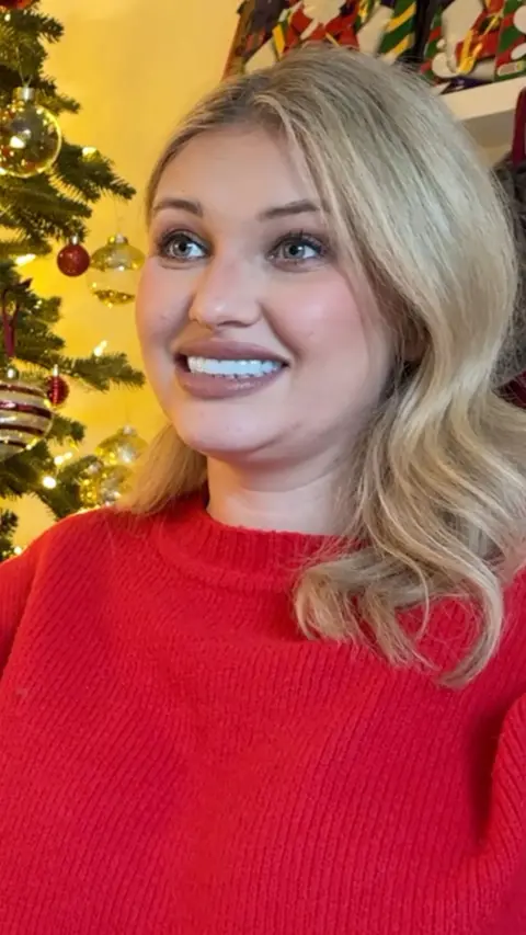 Amy Hart, a blonde woman in a red jumper looks at camera