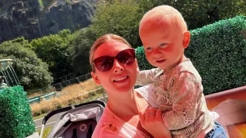 PA Media Aimee King holding her son Corey in front of Edinburgh Castle