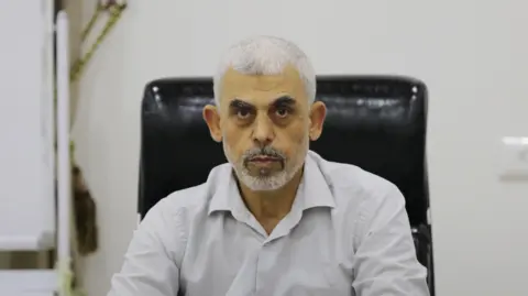 Getty ImagesClose-up shot of Yahya Sinwar, wearing a white shirt, sitting in a black leather desk chair and staring at the camera