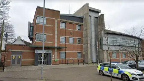 The exterior of Bloxwich Police station. It is a three storey building with a police are parked outside.