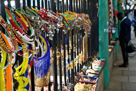 AFP Necklaces featuring colourful beads and metal discs, as well as bracelet and other souvenirs are displayed on municipal railings.