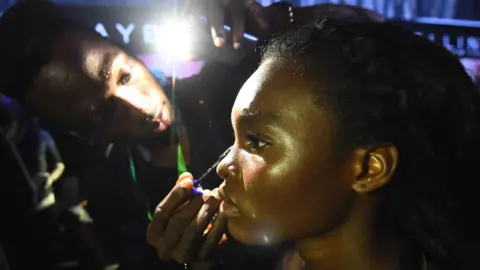 AFP A make-up artist uses a phone's light to prepare a model following an electrical problem during the Lagos Fashion Week - 25 October 2018