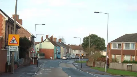 Terry Durbin A road through houses and with a street sign saying 'elderly people'