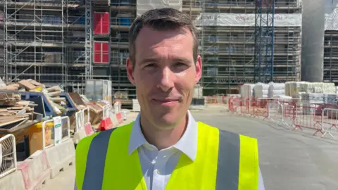 Matthew Pennycook stands on a building site in high-vis vest 