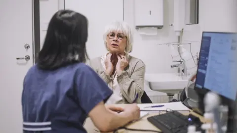 Getty Images Older female patient sits opposite female doctor, describing her symptoms of neck pain