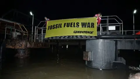 Fionn Guilfoyle/Greenpeace Greenpeace activists scale part of terminal in Grays with banner reading fossil fuels war