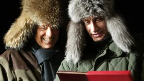 Associated Press Russian President Vladimir Putin presents a book to then Italian President Silvio Berlusconi. Both wear large fur hats.