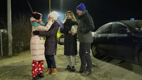 four family members in winter clothing being reunited on a snowy pavement