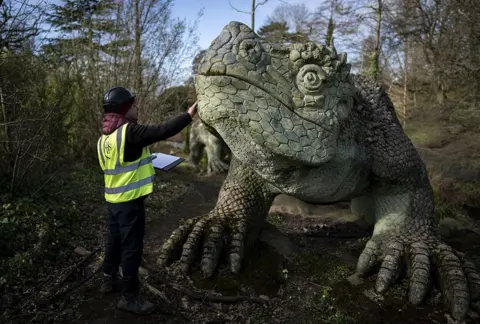 Aaron Chown / PA Media Conservator Pedro Jimenez takes part in conservation work on the 170-year-old dinosaurs that inhabit Dinosaur Island in Crystal Palace Park in south London, 27 March 2023