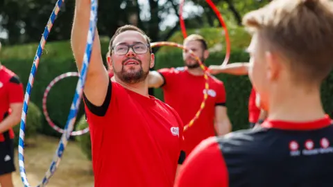 Active Fusion A group of coaches in red shirts spinning hula hoops around their arms.