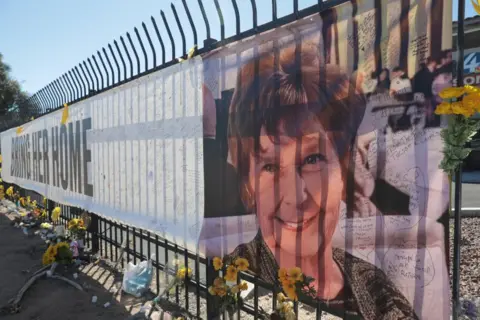 Getty Images A long banner is attached to some black railings, with flowers also laid at its base. The words 'BRING HER HOME' are emblazoned on the banner with the face of Nancy Guthrie on the right hand side