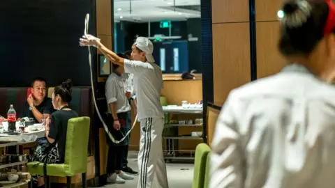 Getty Images A waiter pulls noodles for customers. Haidilao is China's most famous hotpot catering brand known its delicate service.