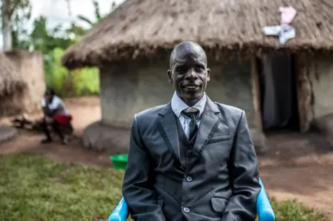 Aurelie Marrier d’Unienville/Sightsavers Simon Peter Otoyo sits outside his house in a blue chair