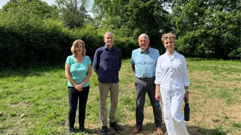 A small field near Blindley Heath. Trees and plants in the background. In the foreground are four people. From left to right, Catherine Sayer, Terry Morgan, Mike Crane and Liz Moor.