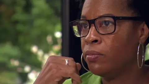 Carolyn Small, mid-speech wearing glasses and silver hoop earrings