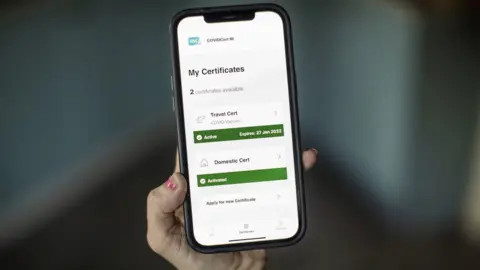 PA Media A person holding a mobile phone which shows a Covid-19 vaccination certificate