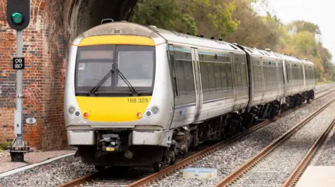 A chiltern class 168 travelling on the newly built east west rail route. It is travelling under a red brick bridge.