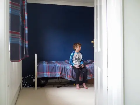 BBC William sitting on his bed, playing computer games