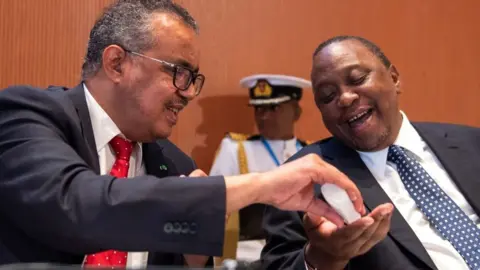 AFP Dr Tedros giving President Kenyatta hand gel. Kenyatta is smiling.