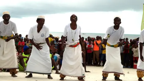 Catherine Tilke Alongside, men wearing white kikoi dance to entertain those who turned out at the finish line