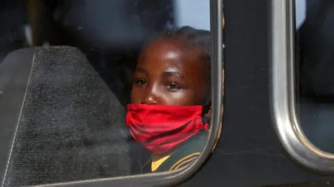 Reuters A girl wearing a mask looks on through a bus window in Eikenhof, south of Johannesburg, South Africa. Photo: August 2020