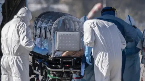 Getty Images Medical workers move a patient with Covid-19 by plane